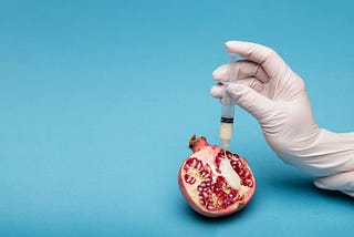 Person Holding Sliced Pomegranate Fruit And Injecting A needle