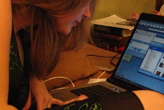 photo of a teen girl looking at a laptop. face mostly obscured. brown hair, pale skin. laptop shows several open windows.
