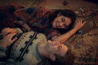 Dex (Leo Woodall) and Em (Ambika Mod) lie on a carpet near Christmas, laughing, in One Day.