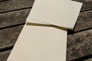 Two sheets of cream-coloured letter-writing paper on a wooden bench.