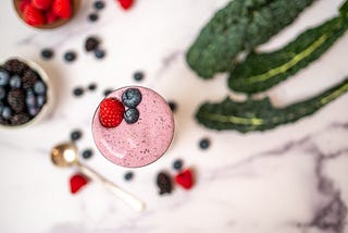 A smoothie surrounded by berries and kale.