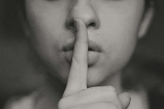 A woman holding a finger in front of her mouth to imply “silence”