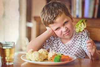 Portrait of a disgusted little boy refusing to eat his vegetables at the dinner table
