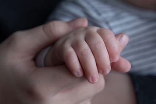 An adult’s hand grasping a child’s hand.