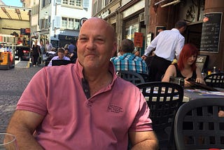 A photograph of Uncle Peter at a street cafe with buildings in the back