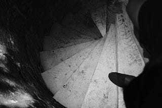 A top-down view of a spiral staircase with worn stone steps, partially illuminated