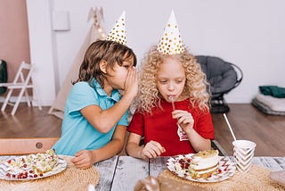 A young boy whispering to a young girl at a party.