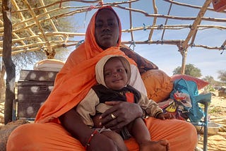 Adiza* mère de famille déplacée, assise avec son enfant sous un hangar.. Photo : PAM/ Aboubacar Sidibé