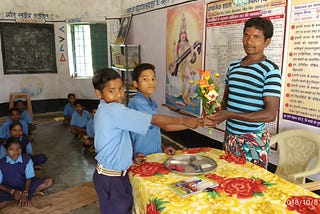 Image is from the event Samman Samaroh. The image shows a student standing on the left handing over a bouquet to a staff