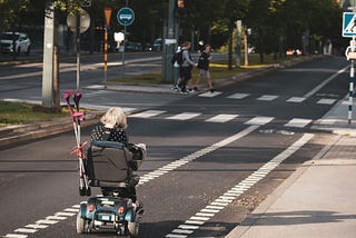 A girl in a black jacket, riding on a black and gray stroller on a road during the day