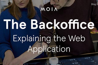 A woman and a man point to a display that shows some metrics. There is text added to the image, it reads: The Backoffice — Explaining the Web Application