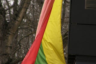 A flags hangs from a balcony. Its colors are yellow, green, & red.