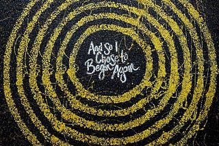 Concentric yellow circles on black background with words “And so I chose to begin again” in the center.