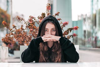 Young woman in black hoodie looking straight with a plant behind her