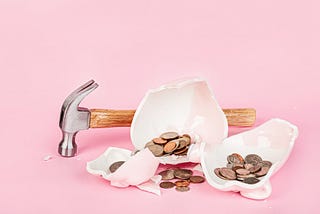 Broken piggy bank — pink background — hammer