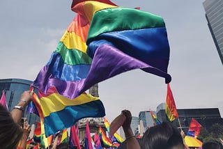 Rainbow flags are waved above the heads of protestors at a crowded Pride march