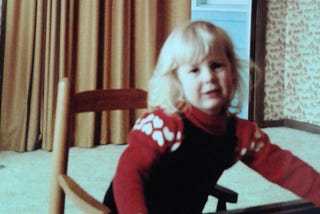 Pic of author when she was two-years old, sitting in a rocking chair in a red sweater.