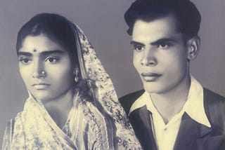 A woman in a floral sari, left, wears a nose ring and a bindi on her forehead. A man in a suit, right, looks straight into the camera.