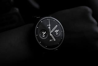 A Moto brand smartwatch shot in the dark, highlighting analogue clock with metrics like notifications & weather on watch face