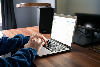 A person writing a blog article on a laptop on a brown desk