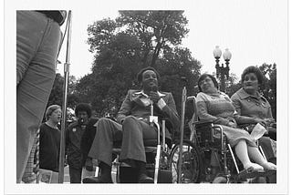 Several disabled activists gathered together. At the center is Brad Lomax, a Black disabled activist.