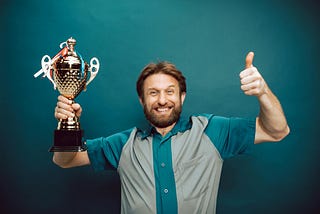 Smiling man holding a trophy and giving the thumbs up.