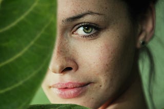 A woman’s face, half-obscured by a large green leaf.