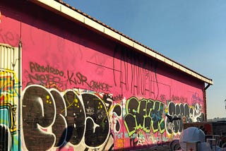 Street art graffiti along a pink-sided warehouse wall