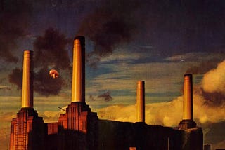 A pig ascends above a factory at sunset.