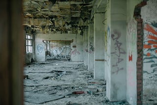Photograph of a crumbling cement building with damage and multicolored graffiti painting on the walls.