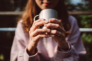 Close-up of a lady’s hands holding a coffee cup outdoors