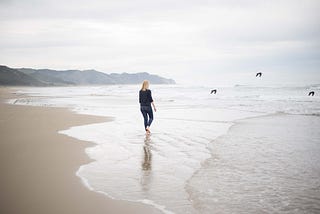 A young woman walking on the beach, and watching birds flying away