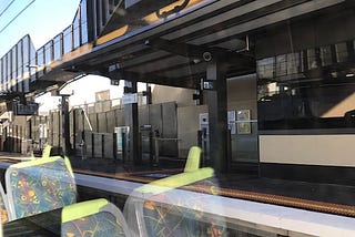 a train station stop through a train window with reflection of train carriage seats in view