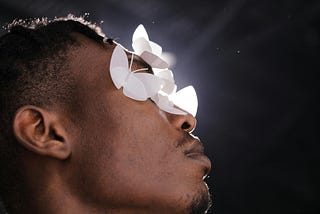 A Black man has paper butterflies over his eyes.