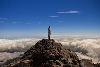 Man standing on mountaintop looking out over the clouds.