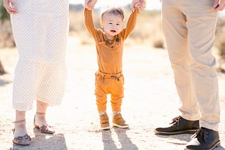 Toddler supported by parents’ hands in desert