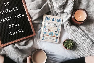 Image of cozy elements including the book ‘Hygge,’ a candle, cup of coffee, and motivational quote, symbolizing happiness in Denmark.