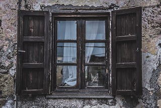 Cat watching out an old window with weathered shutters