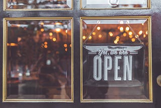 “Yes, we are OPEN” sign hanging in glass window of door