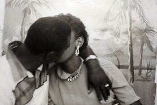 A Black couple kissing in front of a beach themed back drop