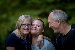 Family embracing a man with down syndrome and smiling to each other.