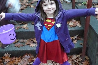 Girl wearing a Superman costume and holding a purple pumpkin container