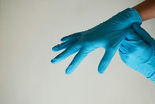 Two hands in blue latex or nitrile medical gloves against a white background.