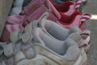 Five pairs of children’s shoes stand empty in a line.