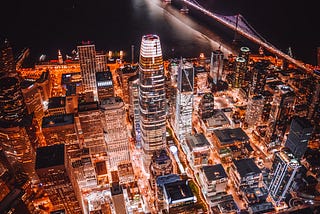 A bird’s eye view of Downtown San Francisco at night. The Salesforce tower is in the center of this evening shot with the Bay Bridge in the background.