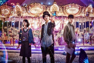Netflix show “The Sound of Magic” is based on a Webtoon called “Annarasumanara” by creator Kim Sung-Youn. The poster’s picture is in a theme park with a lit-up carousel behind our three main characters. There’s bubbles floating in the foreground. The magician is in the center holding a blue butterfly. Our female MC is on one side and the male MC on the other.