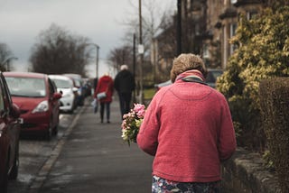 elderly woman carrying a bouquet of flowers while walking down the street