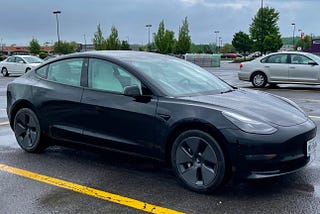 Black tesla model 3 car with white seats in a parking lot on a rainy day