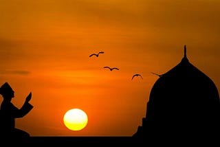 A boy is praying outdoor in front of a mosque