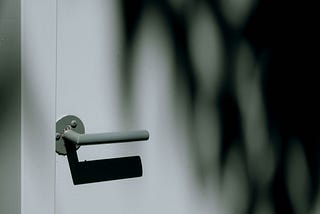 Gray door handle casting a shadow on a light colored door.
